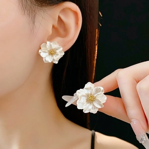 Elegant white floral resin stud earrings with golden pistils worn by a model