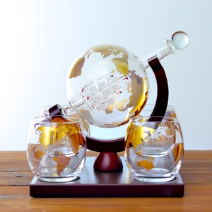 Detailed globe whiskey decanter with sailing ship inside on a dark wood stand with map glasses