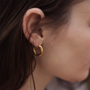 Close-up of chunky gold-plated C-shaped hoop earrings on female model with polished finish