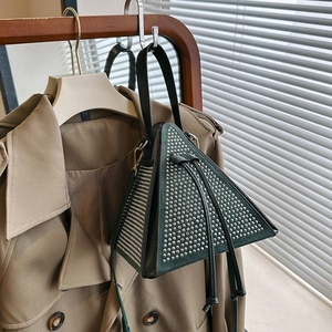 Dark green triangular handbag with silver studs on a stylish trench coat background