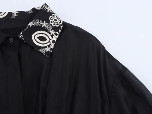 Detail of elegant white floral embroidery on the neckline of a black waist-belted dress
