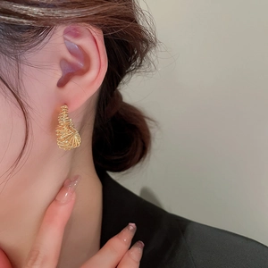 Detail view of champagne gold multilayered wire wrapped cone earrings on model