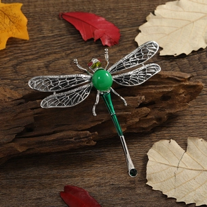 Elegant silver dragonfly brooch with green enamel and emerald-colored gemstones on wood