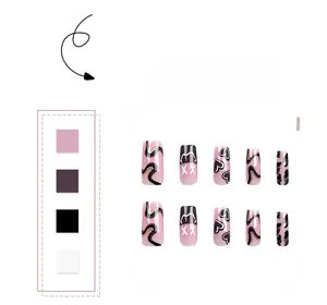 Close-up of pink press-on nails with black swirls, heart patterns and golden glitter trim