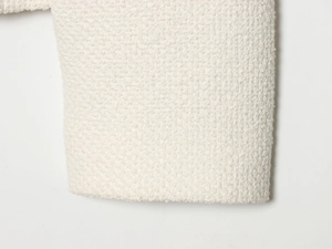 Close-up of white bouclé tweed jacket sleeve showcasing rich fabric texture and weave