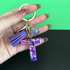 Detail of resin letter T keychain with purple tassel and colorful stones in gold hardware