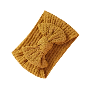 Knitted mustard yellow baby headband with large bow detail on white background