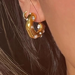 Close-up of a gold C-shaped earring with sparkling zircons on a model's ear