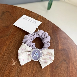 Detail of lavender floral scrunchie with pearl bow and letter A on wooden surface