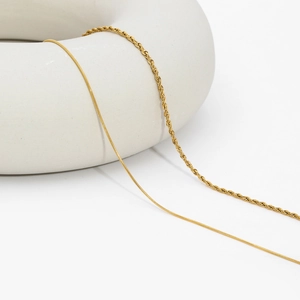 Detailed view of layered gold snake chain and twisted rope necklaces on white ceramic decor