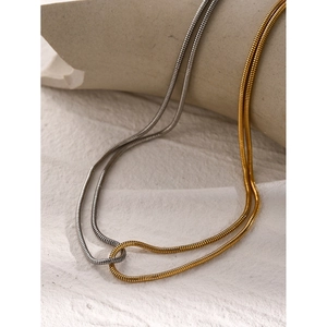 Detailed view of two-tone gold and silver herringbone chains on a beige textured background