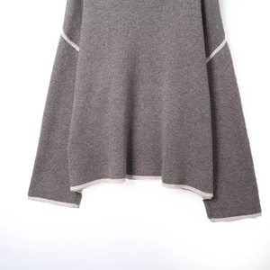 Detail view of grey knit sweater showing white contrast trim on the hem and cuffs