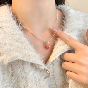 Detail of 18k gold heart pendant necklace with colorful beads on a cozy cream sweater