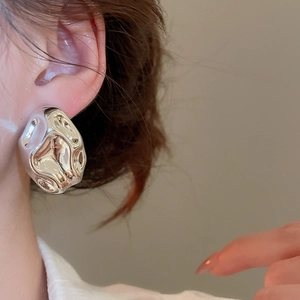 Close-up of a silver irregular lava metal stud earring worn by a female model