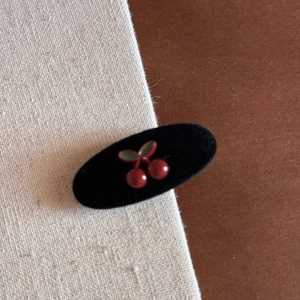 Close-up of a vintage black velvet hair claw clip with a 3D red cherry and green leaf design