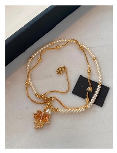 Macro shot of double-layered pearl and gold chain necklace with amber maple leaf charm