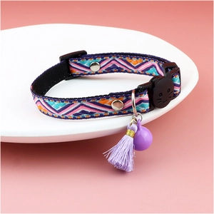 Close-up of cat collar with purple tassel, bell, and cat-shaped buckle on pink background
