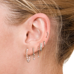 Close-up of elegant silver pearl hoop earrings and zircon studs worn on a model ear