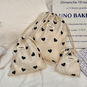 Three sizes of cream drawstring bags with black heart prints and logo labels
