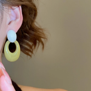 Detail view of retro acrylic earrings with white oval top and olive green ring on model