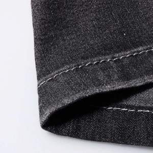 Detailed macro shot showing the fine white stitching on dark gray denim trouser hem