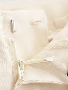 Close-up of metal zipper and hook closure on cream high-waisted casual trousers