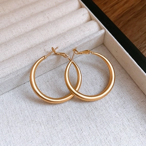 Macro detail of matte gold C-shaped hoop earrings on a velvet display tray