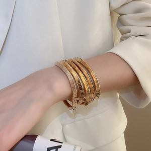 Close-up of layered gold metal cuff bracelet with horizontal textures worn on wrist