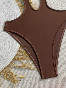 Detail of dark brown ribbed one-piece swimsuit with high-cut leg and white straw hat