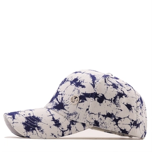 Detail of blue and white tie-dye baseball cap featuring a metal M letter logo on the side