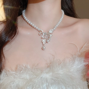 Detail view of a vintage pearl necklace with a diamond bow pendant worn by a model