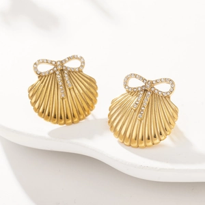 Macro shot of gold shell earrings with rhinestone bow accent on a white textured stand