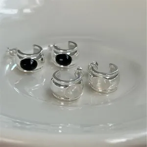 Detail of C-shaped silver earrings with black onyx and white opal inlay on white ceramic