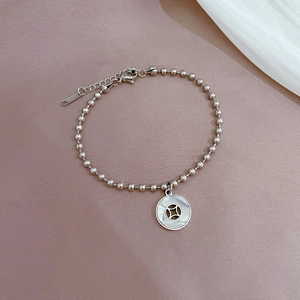 Detailed shot of silver beaded bracelet with a shell coin pendant on a soft background