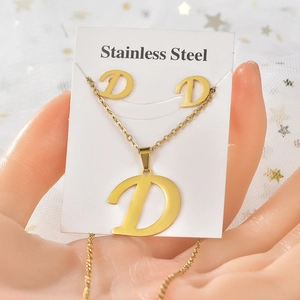 Dettaglio macro del set di gioielli in acciaio dorato con collana e orecchini lettera D