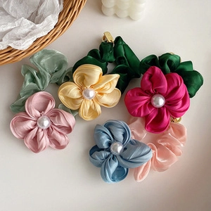 Detailed close-up of colorful satin flower scrunchies with pearls on white background