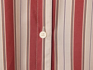 Détail macro du tissu d'une chemise à rayures rouges et beige avec bouton blanc