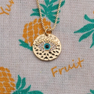 Vue macro du collier pendentif œil maléfique plaqué or avec texture martelée et zircons