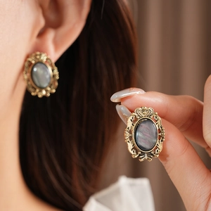 Close-up of vintage bronze earrings with dark oval resin stone and ornate filigree detail