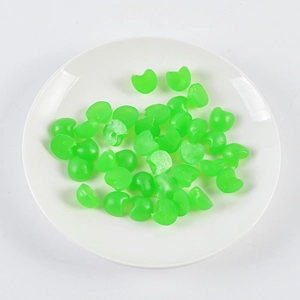 Macro view of mini green heart-shaped resin beads for DIY crafts in a white dish