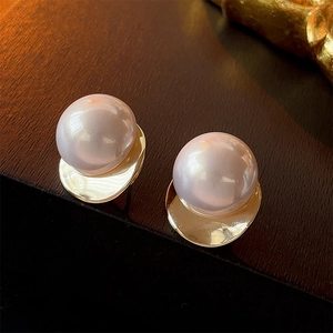 Macro shot of large pearl earrings with gold irregular metal base on a wood background