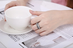 Close-up of unisex brushed stainless steel ring with black stripe on a hand holding a cup