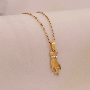 Golden palm pendant necklace with mini pearls on soft beige fabric background