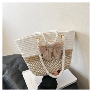 Detail of woven straw tote bag with white cotton rope handles and beige bow decoration