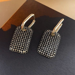 Gros plan sur des boucles d'oreilles créoles dorées avec pendentifs noirs rectangulaires