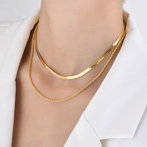 Detail of layered gold herringbone and rope chains worn on a white blazer outfit