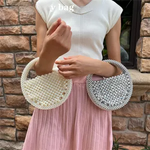 Detail view of woven beaded half-moon handbags in pearl and silver rhinestone finishes