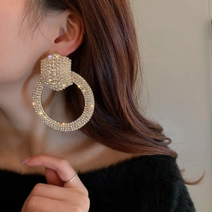Close-up of sparkling full-rhine stone large hoop earrings worn by a model in gold finish