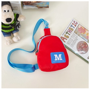 Détail du sac bandoulière enfant en nylon rouge avec sangle bleue et écusson lettre M