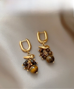 Detailed close-up of 18k gold bird earrings featuring brown tiger eye stone tassels